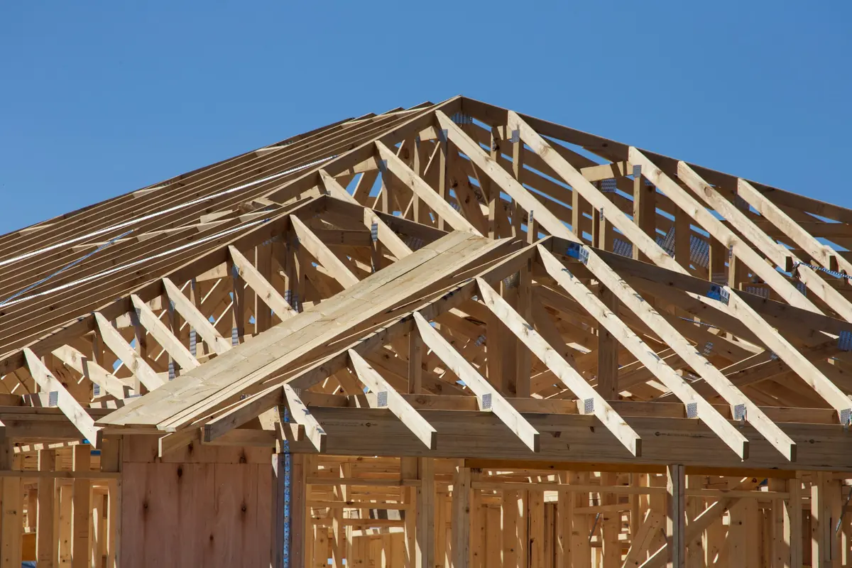 New house under construction with timber wall framing and roof trusses against a clear blue sky