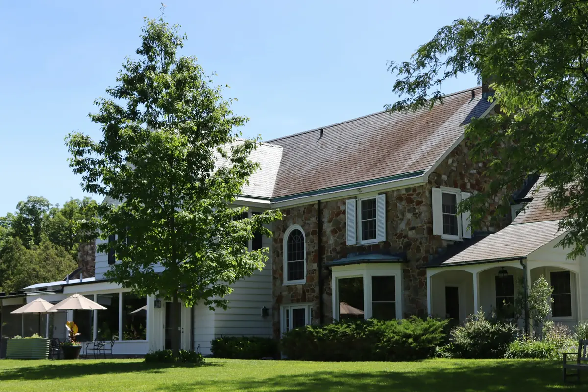 Stone and white clapboard country house with arched window, dormers, mature trees and manicured lawn