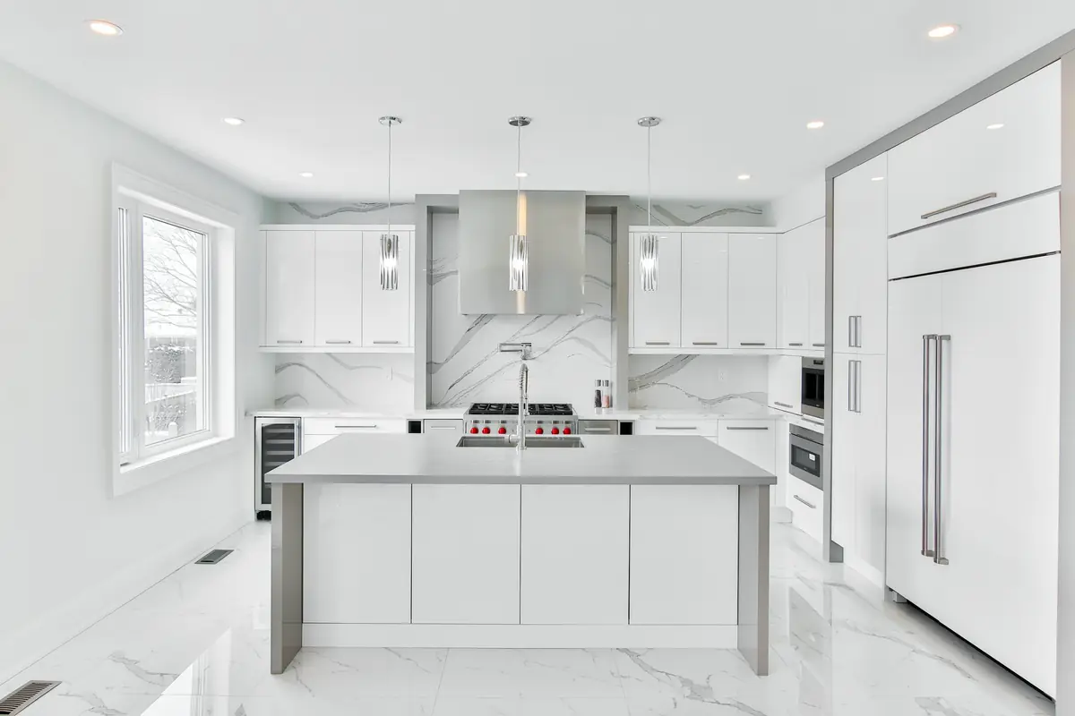 Bright white kitchen with flat-panel cabinetry, central island, stainless range hood, pendant lights and marble backsplash