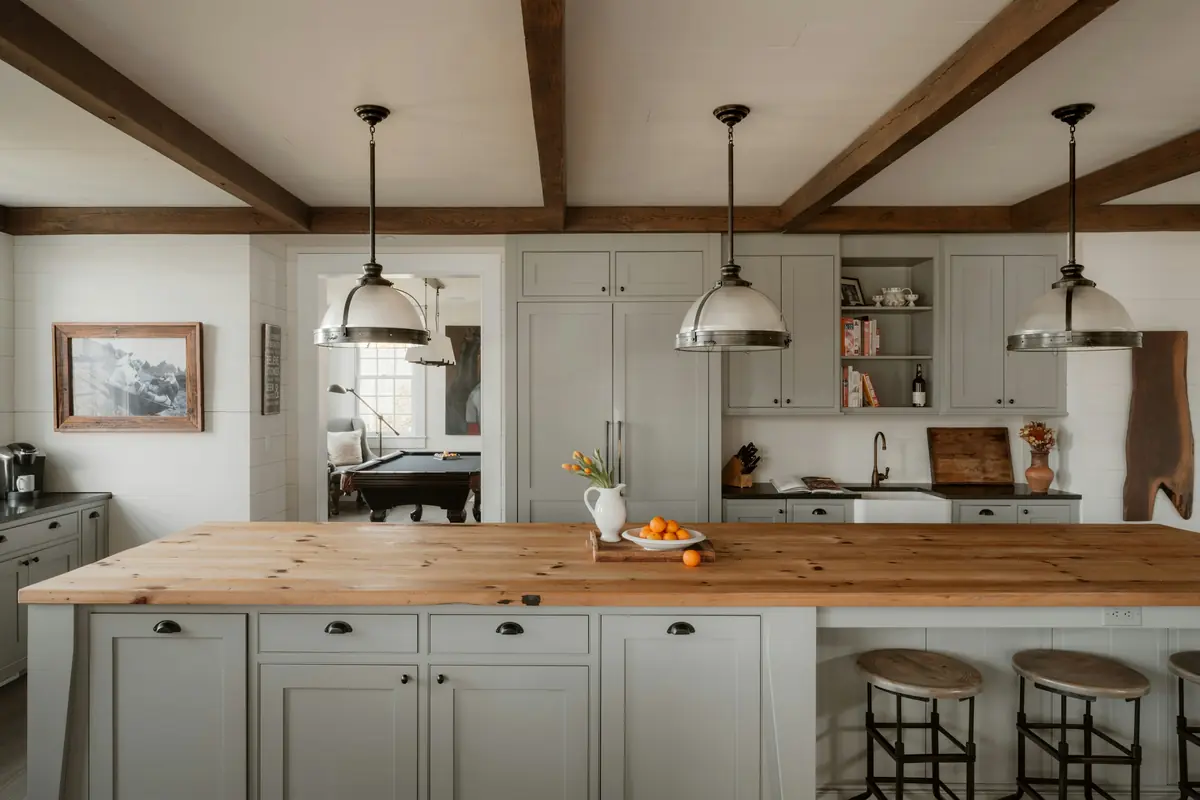 Farmhouse kitchen with exposed wood beams, butcher-block island, sage shaker cabinets and nickel pendant lights