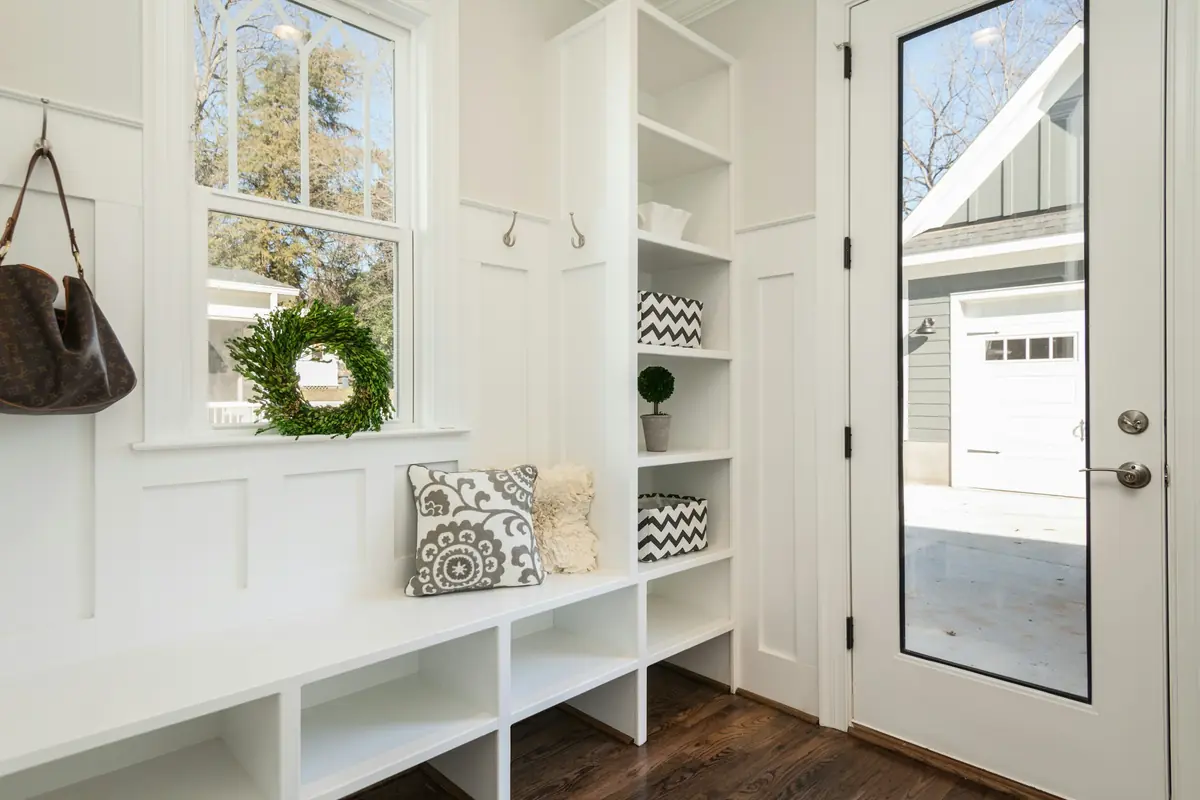 White mudroom with built-in bench, cubbies, coat hooks, board-and-batten walls and glass back door