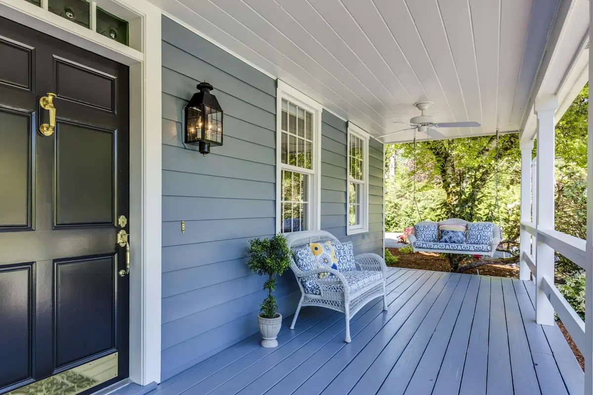 Covered front porch with black paneled door, brass hardware, lantern, blue-gray floor and wicker seating